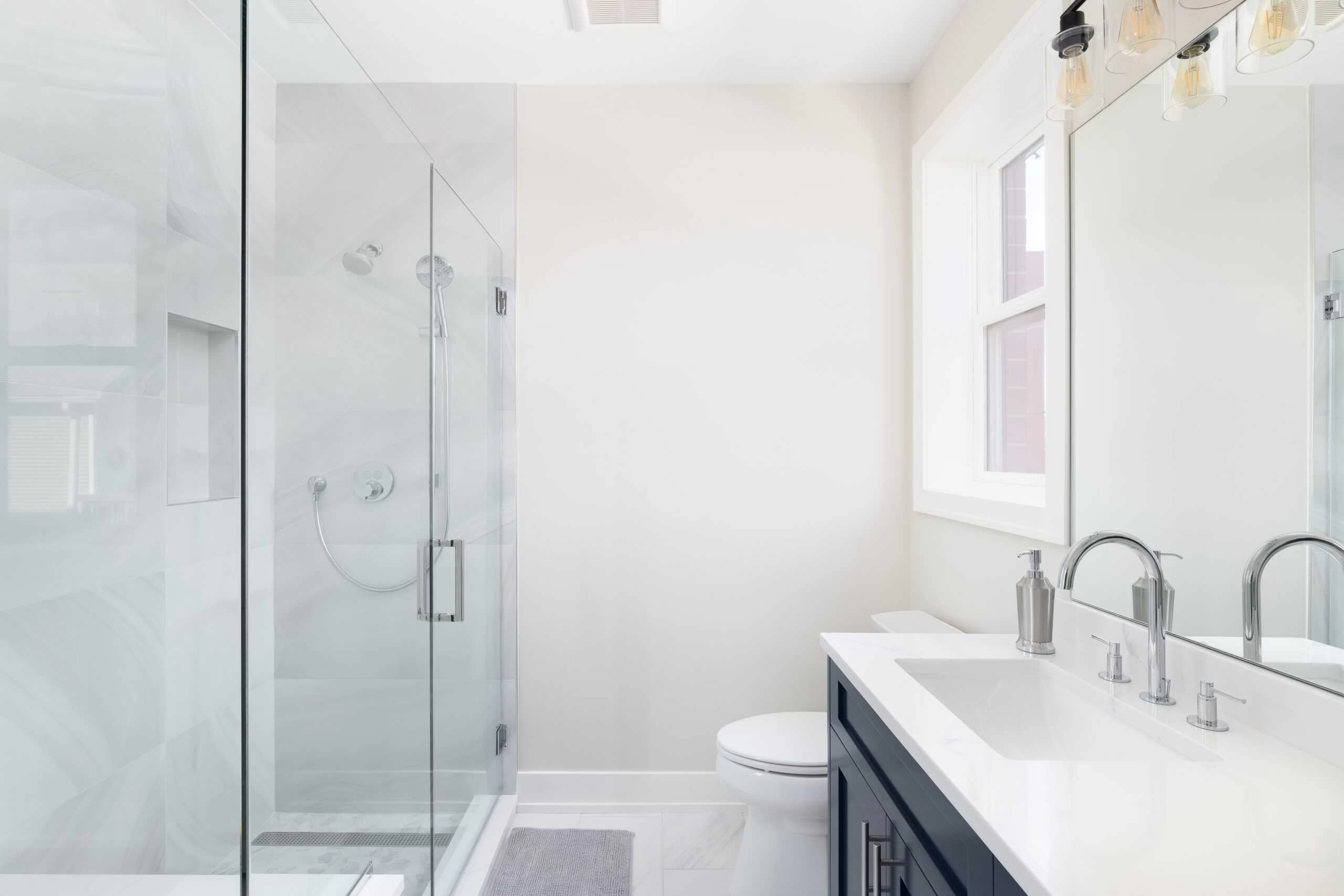 Modern bathroom with glass-enclosed shower, white walls, and vanity with dual sinks and mirrors.