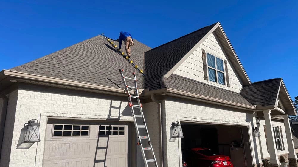 A man on a ladder cleaning the roof of a house.