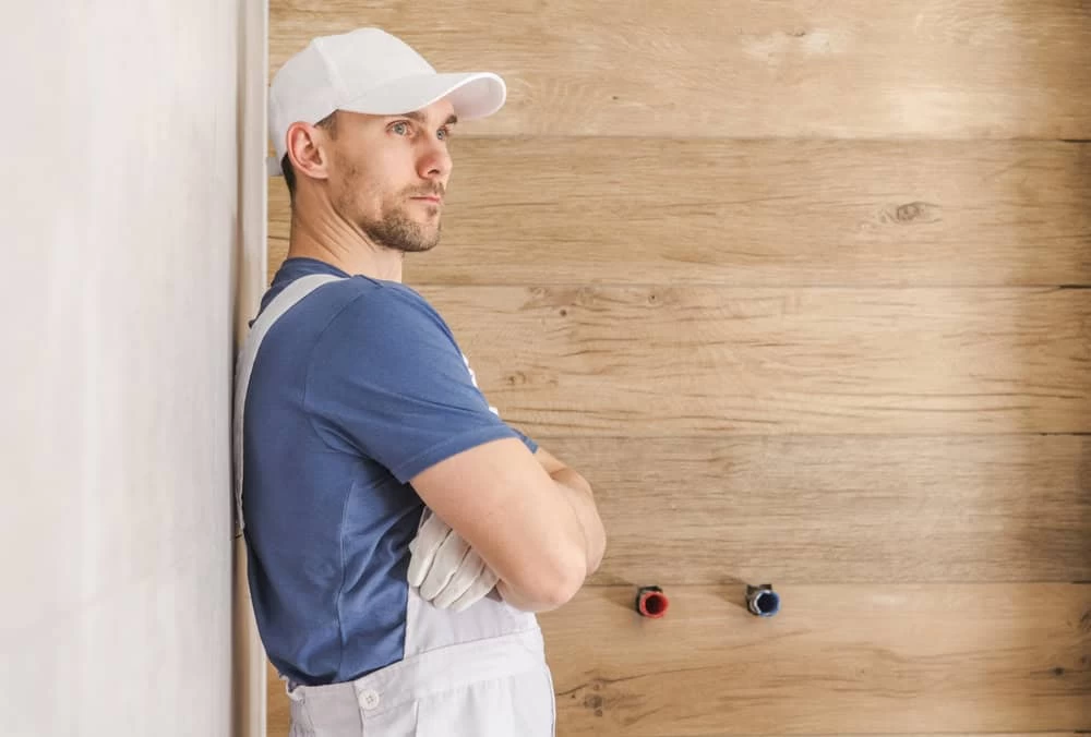 A man in a white hat and overalls stands in front of a wall.