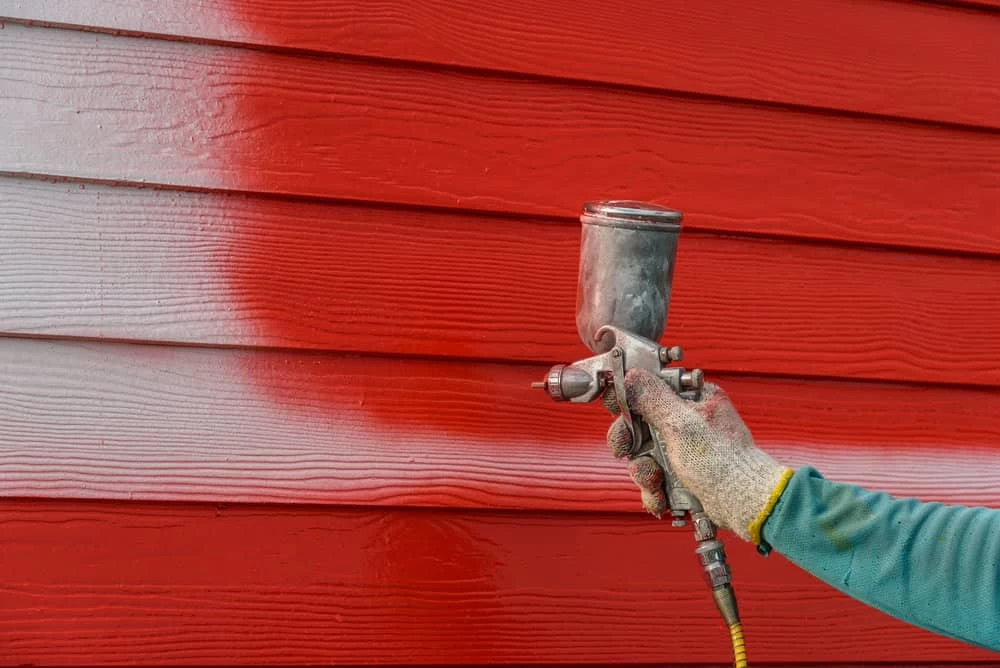 A person is painting a red house with a spray gun.