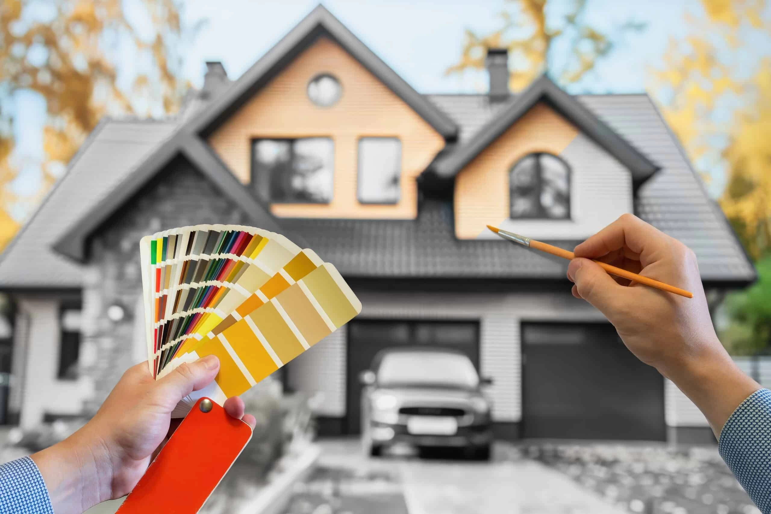 A person holding a paintbrush and a paint sample in front of a house.